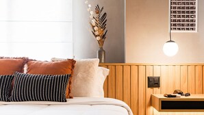 Ein ordentlich bezogenes Bett mit weißer und brauner Tagesdecke, eine Vase mit getrockneten Blumen und ein Nachttisch mit einer Lampe.