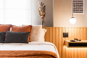 Ein ordentlich bezogenes Bett mit weißer und brauner Tagesdecke, eine Vase mit getrockneten Blumen und ein Nachttisch mit einer Lampe.