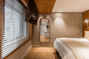 Ein Schlafzimmer mit einem Bett, einem Spiegel, einem an der Wand befestigten Fernseher und einem Fenster mit Jalousien.