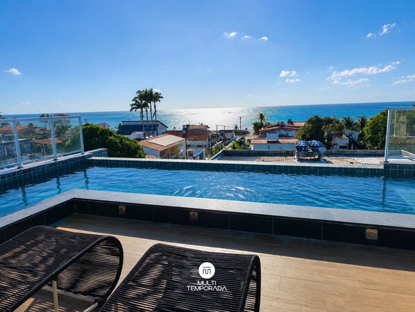 A rooftop infinity pool with a view of the ocean and a cityscape. - Flat Miray Exclusive com Piscina (Tamandaré)