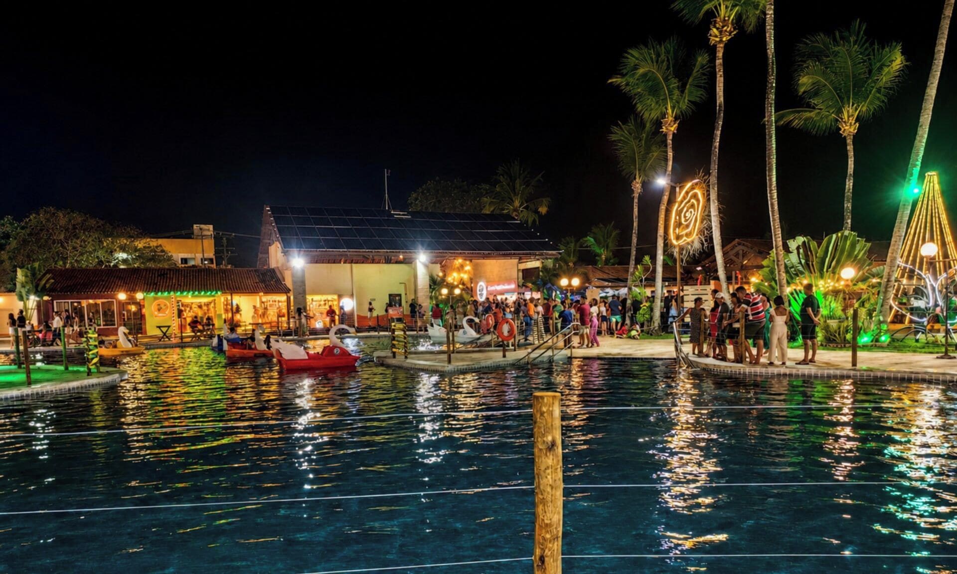 Ein Poolbereich bei Nacht mit Booten, Palmen und einem Gebäude mit Beleuchtung.