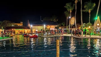 Ein Poolbereich bei Nacht mit Booten, Palmen und einem Gebäude mit Beleuchtung.