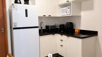 Eine kleine Küche mit einem weißen Kühlschrank, einer Mikrowelle, einer Kaffeemaschine und einem Toaster.