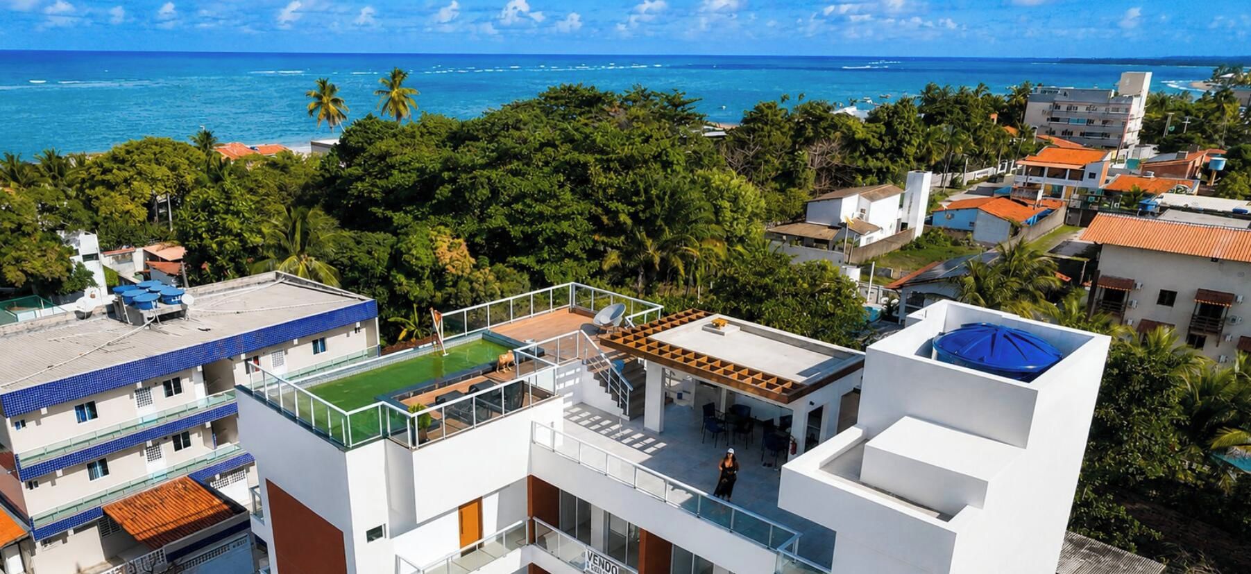 Un edificio moderno con piscina en la azotea, rodeado de exuberante vegetación y vistas al océano.
