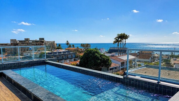 An infinity pool with a clear view of the ocean and buildings in the background. - Flat Miray Exclusive com Piscina (Tamandaré)