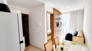 A hotel room with a dining area, a bed, a wardrobe, and a window with curtains. - Flat Miray Exclusive com Piscina (Tamandaré)