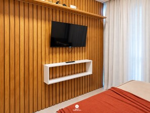 A room with a television mounted on a wooden wall, a white shelf below it, and a bed with a red blanket. - Flat Miray Exclusive com Piscina (Tamandaré)