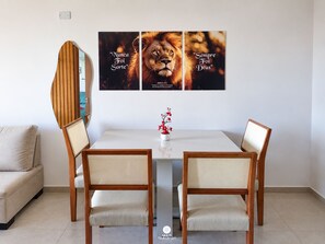 A dining area with a white table, two wooden chairs, and a wall-mounted artwork featuring lions.