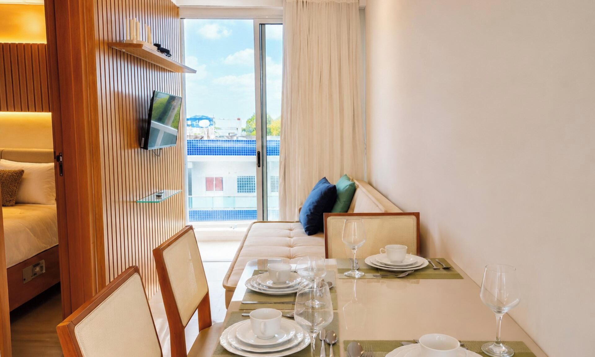 Hotelkamer met een zithoek, een bank, een televisie en uitzicht op een blauw gebouw door een glazen deur.