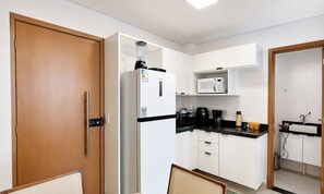 Una cocina compacta equipada con refrigerador, microondas, cafetera y un lavamanos pequeño.