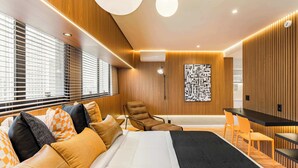 A modern hotel room with a bed, a seating area with chairs, a desk, and a large window with blinds. - Cyclinn a 400m do WTC Berrini Vila Olímpia #WB1101 (Berrini)