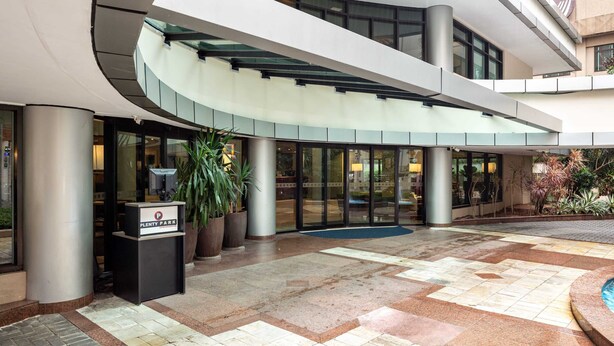 A modern building with a curved entrance, a reception desk, and a glass door leading inside. - Cyclinn a 400m do WTC Berrini Vila Olímpia #WB1101 (Berrini)