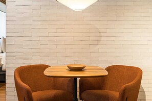 A room with a white brick wall, a round wooden table with a bowl, and two brown upholstered chairs. - Cyclinn a 400m do WTC Berrini Vila Olímpia #WB1703 (Berrini)