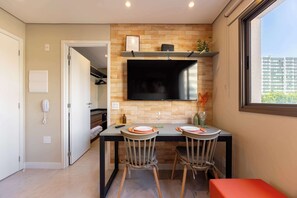 A modern kitchen with a brick wall, a flat-screen TV, and a dining area with two chairs and a table. - Studio Completo a 500m do Metrô Borba Gato | AD503 (Brooklin)