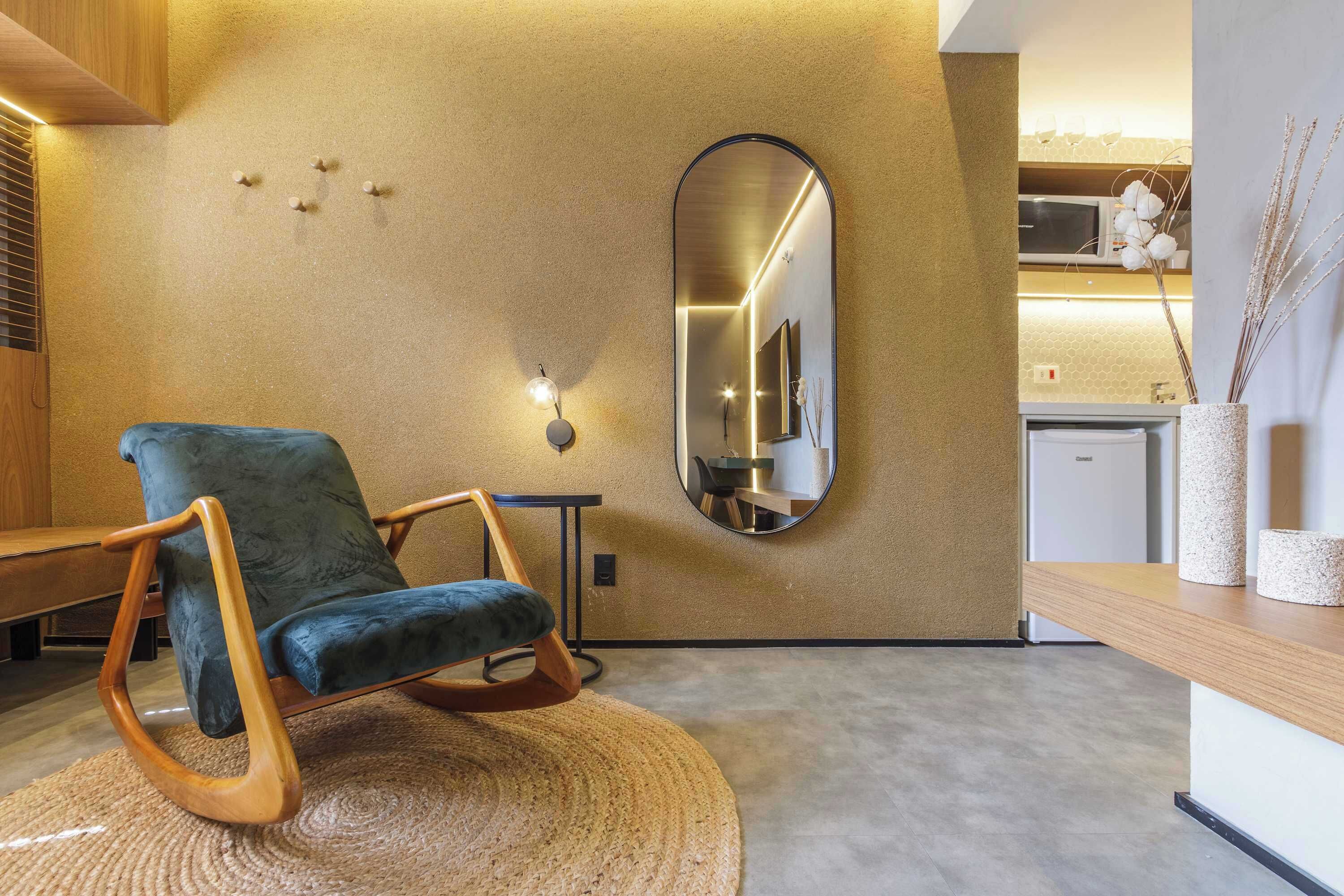 Een modern interieur met een schommelstoel, een ronde spiegel en een keukenhoek.