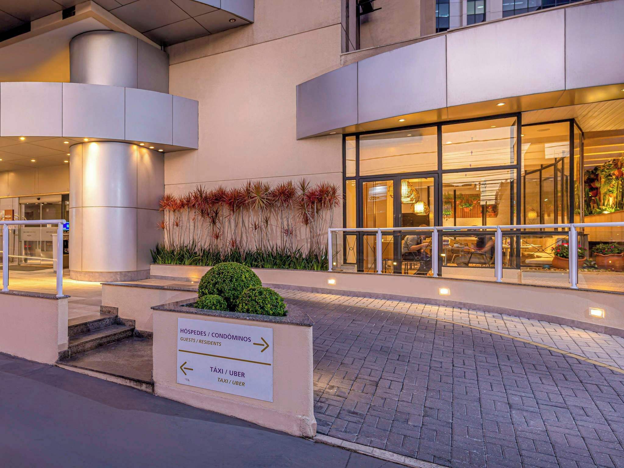 Entrada moderna de hotel, com sinalização indicando direções para quartos e serviços de táxi/uber.
