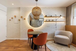 A dining area with a round table, two orange chairs, a round mirror, and a hanging light fixture. - #WP206 | Cyclinn Paulista Jardins (Jardim Paulista)