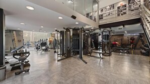 Un gimnasio con diferentes máquinas de ejercicio, una escalera y un entrepiso con barandilla.