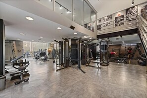 Ein Fitnessstudio mit verschiedenen Trainingsgeräten, einer Treppe und einer Empore mit Geländer.