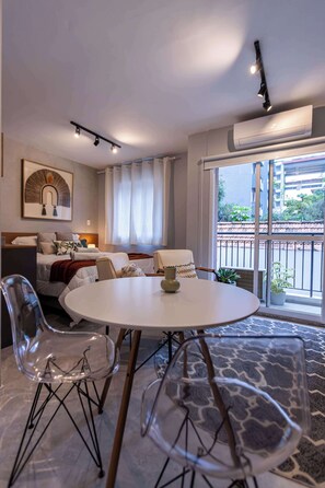 A modern hotel room with a bed, a dining table, chairs, a sofa, and a balcony with a view. - Studio Completo a 10min do H das Clínicas | PP210 (Pinheiros)