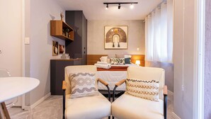 Una camera d'albergo con un letto, due poltrone, un tavolino, uno scaffale con soprammobili e un quadro appeso al muro.