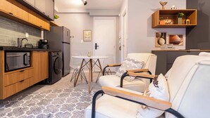 Una cucina moderna con lavastoviglie, forno a microonde e frigorifero, una zona pranzo con tavolo e sedie, e un angolo salotto con divano e poltrone.