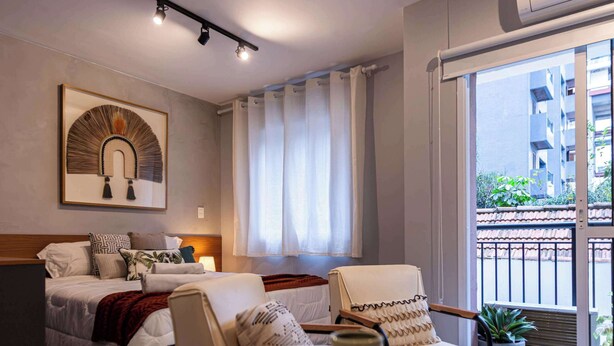 Una camera d'albergo con un letto, un comodino, una lampada, una pianta in vaso e vista all'esterno.
