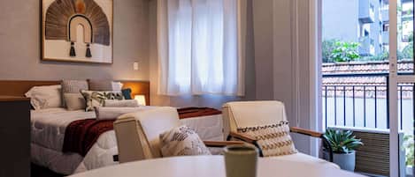 Una habitación de hotel con cama, mesita de noche, lámpara, planta en maceta y vistas al exterior.