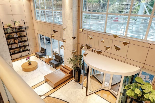 Un hall d’entrée spacieux avec un plafond haut, un coin salon avec des canapés, une table basse et une bibliothèque agrémentée d’objets décoratifs.