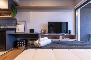 A modern bedroom with a bed, a TV, a desk, and a small kitchenette. - Studio Completo a 5min do Metrô Madalena | HV108 (Vila Madalena)