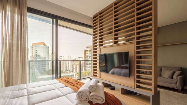 A modern hotel room with a large bed, a TV, a wooden slat wall, and a view of the city. - #VN1609 | Cyclinn Vila Olímpia (Vila Olímpia)