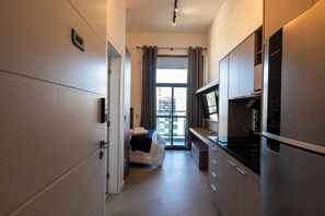 A compact kitchen with a refrigerator, stove, and a small dining area with a chair and table. - Studio Completo a 100m do Metrô Brooklin | HM1113 (Brooklin)