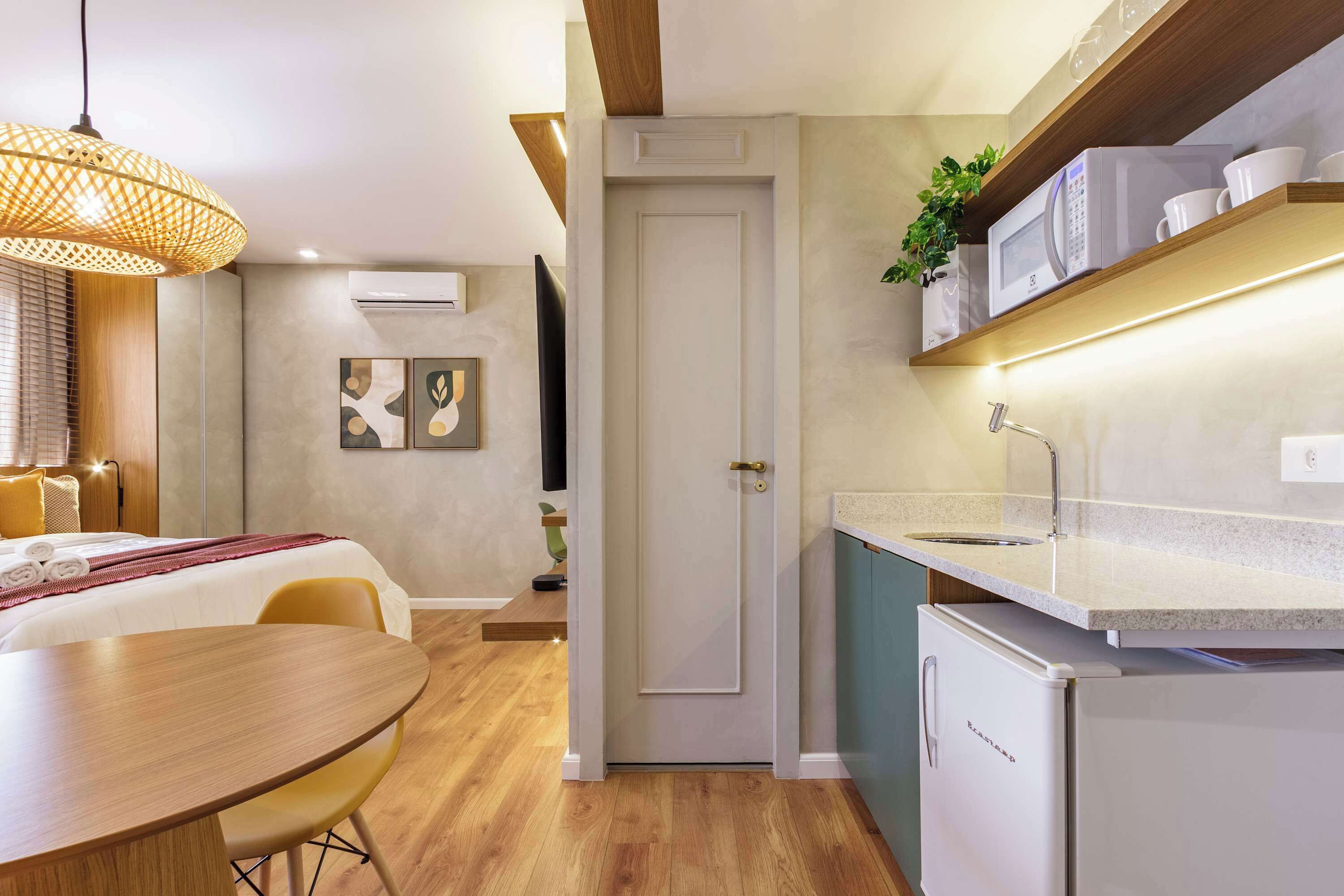 A compact hotel room with a dining area, kitchenette, and a door leading to another room.