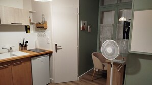 Eine kleine Küche mit Geschirrspüler, Spüle und einer Holzarbeitsplatte. Es gibt einen Essbereich mit einem Stuhl und einem Tisch, sowie einen Standventilator.