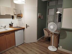 A compact kitchen with a dishwasher, a sink, and a wooden countertop. There is a dining area with a chair and a table, and a standing fan. - Le Petit Jean Alexandre – Studio centre-ville (Poitiers)