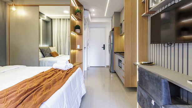 Moderni hotellihuone, jossa on sänky, televisio, pieni keittiö ja kylpyhuone.