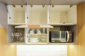 A kitchen with a microwave, glassware, and plates on shelves. - Studio Completo a 5 min do Nubank Parque | MP302 (Perdizes)