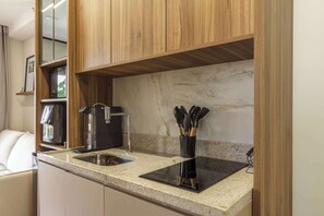 A kitchen with wooden cabinets, a granite countertop, a black induction cooktop, a coffee maker, and a sink. - Studio Completo a 5min do Allianz Parque | GP33 (Perdizes)