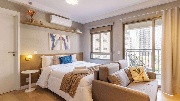Ein modernes Hotelzimmer mit Bett, Sofa, Nachttisch, Kunstwerk und einem Balkon mit Blick.