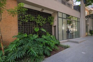 A modern building with a brick facade, a glass entrance, and a green wall with plants. - Studio Completo a 5 min do Nubank Parque GP94 (Perdizes)