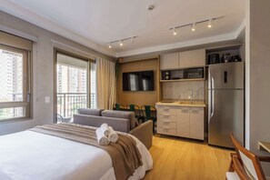 A hotel room with a bed, a sofa, a dining table, a TV, a microwave, and a refrigerator. - Studio Completo a 5 min do Nubank Parque GP94 (Perdizes)