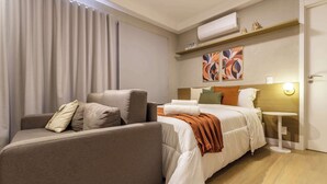 A hotel room with a sofa, a bed with white bedding, a small table with a lamp, and an air conditioning unit on the wall. - Ape Pet Friendly a 5 min do Nubank Parque GP55 (Perdizes)