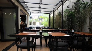 An indoor dining area with tables and chairs, large windows, and indoor plants. - Flat a 300m do Metrô Consolação | BC1108 (Bela Cintra)