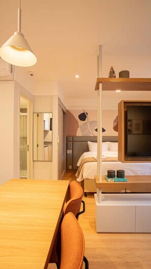 Ein modernes Hotelzimmer mit einem Holztisch, einem Einzelbett, einem großen Spiegel und einem Fernseher auf einem Holzbalken.