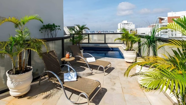 A rooftop pool area with lounge chairs, potted plants, and a clear view of the city skyline. - Flat a 300m do Metrô Consolação | BC1108 (Bela Cintra)
