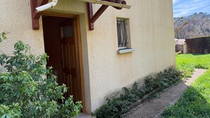 A building with a wooden door, a window with a metal frame, and a small garden area with greenery and a gravel path. - The House of Seasons (Apt)