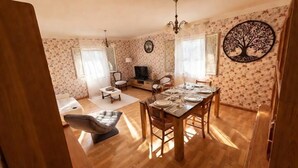 A dining area with a wooden table set for four, a sofa, a TV, and a chandelier. - The House of Seasons (Apt)