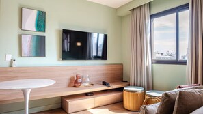 A modern hotel room with a flat-screen TV, a small table, a sofa, and a window with curtains. - Flat a 300m do Metrô Consolação | BC1505 (Bela Cintra)