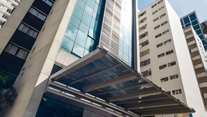 A modern high-rise building with a prominent glass facade and a unique cantilevered entrance. - Flat a 300m do Metrô Consolação | BC1505 (Bela Cintra)