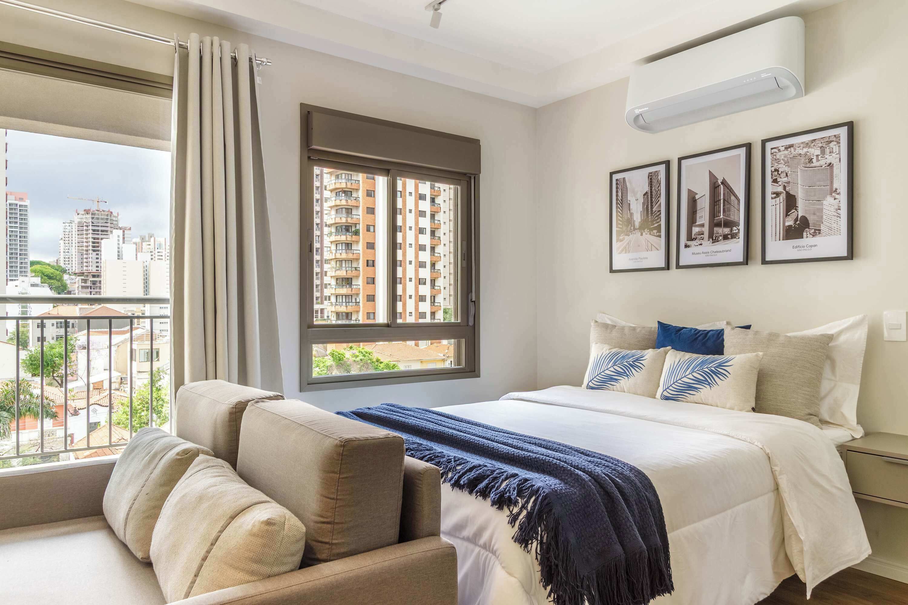 Un dormitorio con una cama grande, un sofá, una ventana con cortinas y vistas a la ciudad.